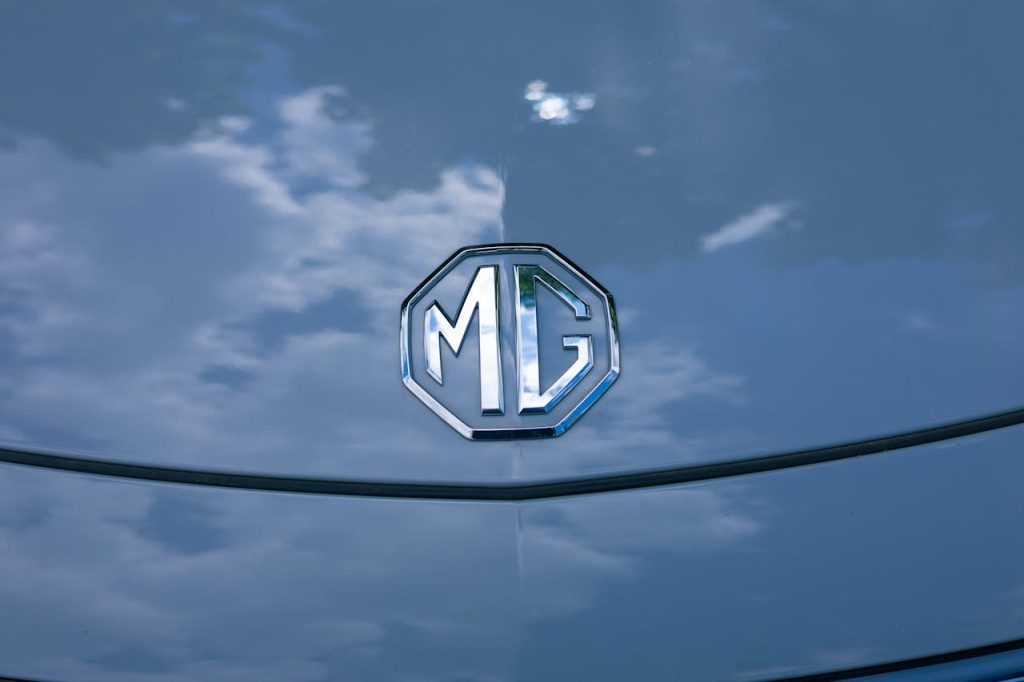 Vibrant MG logo on a car hood with striking sky reflection, symbolizing elegance.