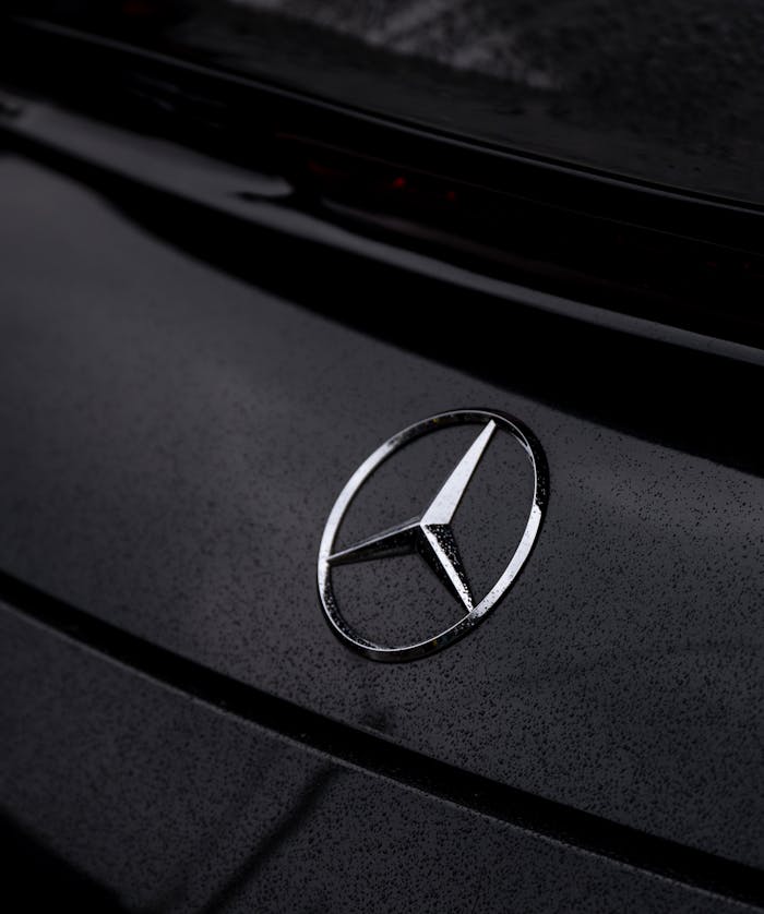 Detailed shot of a Mercedes emblem on a car with rain droplets.